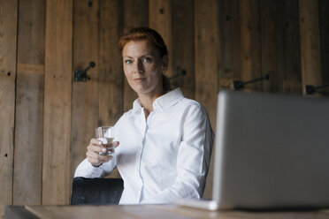 Porträt einer selbstbewussten Geschäftsfrau am Schreibtisch mit einem Glas Wasser und einem Laptop - JOSF03031