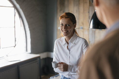 Smiling businesswoman with cup of coffee in office looking at senior man - JOSF03039