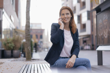 Lächelnde Geschäftsfrau mit Handy im Freien sitzend in der Stadt - JOSF03042