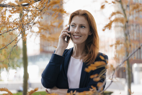 Lächelnde Geschäftsfrau am Handy im Freien in der Stadt im Herbst, lizenzfreies Stockfoto