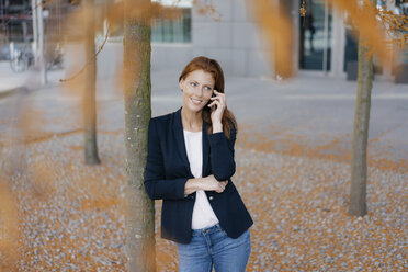 Smiling businesswoman on cell phone outdoors in the city in autumn - JOSF03046