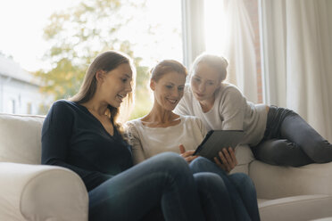 Happy mother with two teenage girls using tablet on couch at home - JOSF03052