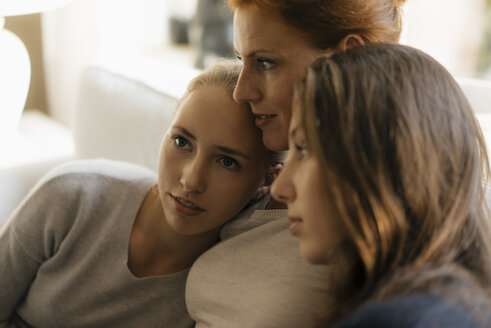 Affectionate mother with two teenage girls on couch at home - JOSF03055