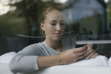 Portrait of serious teenage girl using cell phone on couch at home - JOSF03057