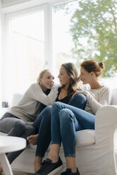 Happy mother with two teenage girls on couch at home - JOSF03062