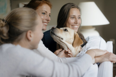 Happy mother with two teenage girls and dog on couch at home - JOSF03063
