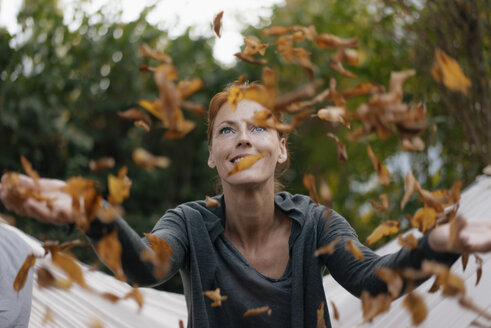 Carefree woman in hammock throwing autumn leaves - JOSF03066