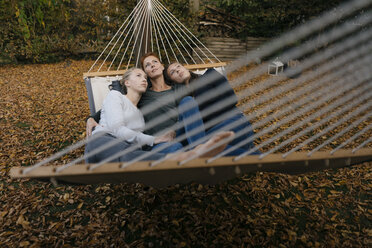 Mutter mit zwei Mädchen im Teenageralter in der Hängematte liegend im Garten im Herbst - JOSF03068