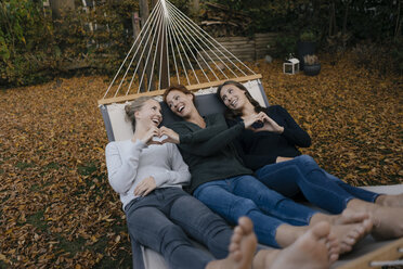 Glückliche Mutter mit zwei Mädchen im Teenageralter in der Hängematte liegend im Garten im Herbst - JOSF03069