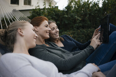 Glückliche Mutter mit zwei Mädchen im Teenageralter liegt in der Hängematte im Garten im Herbst mit Tablet - JOSF03070