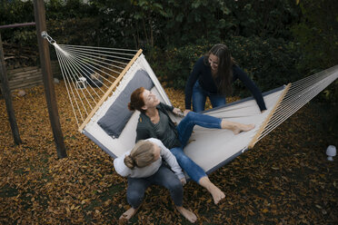 Glückliche Mutter mit zwei Teenager-Mädchen in der Hängematte im Garten im Herbst - JOSF03071