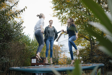 Glückliche Mutter mit zwei Mädchen im Teenageralter, die im Herbst im Garten auf dem Trampolin springen, lizenzfreies Stockfoto