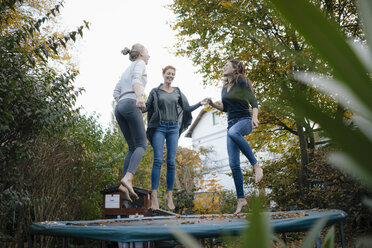 Happy mother with two teenage girls jumping on trampoline in garden in autumn - JOSF03072