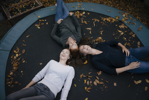 Happy mother with two teenage girls lying on trampoline in autumn - JOSF03073