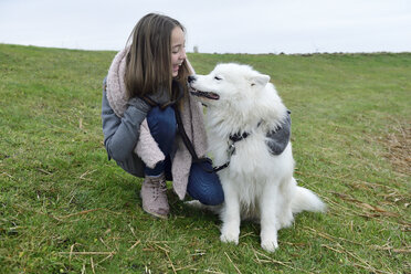 Lachendes Mädchen, das mit seinem Hund auf einer Wiese hockt - ECPF00250