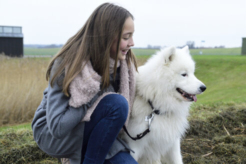 Lächelndes Mädchen, das neben ihrem Hund auf einer Wiese hockt - ECPF00252