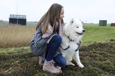 Lachendes Mädchen, das neben ihrem Hund auf einer Wiese hockt - ECPF00253