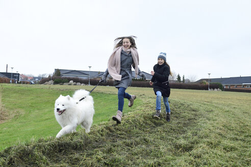 Zwei Mädchen laufen auf einer Wiese mit Hund und haben Spaß - ECPF00255
