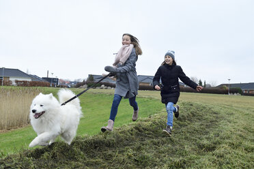 Zwei Mädchen laufen auf einer Wiese mit Hund und haben Spaß - ECPF00256