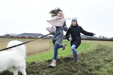 Zwei Mädchen laufen auf einer Wiese mit Hund und haben Spaß - ECPF00257