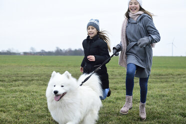 Zwei Mädchen laufen auf einer Wiese mit Hund und haben Spaß - ECPF00259