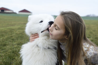 Mädchen und ihr weißer Hund kuscheln auf einer Wiese - ECPF00260
