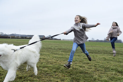 Zwei Mädchen laufen auf einer Wiese mit Hund und haben Spaß - ECPF00262