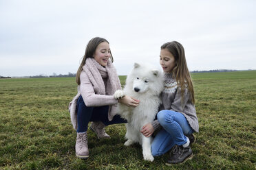 Two girls crouching on a meadow teaching dog - ECPF00264