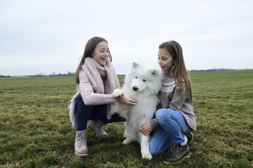 Zwei Mädchen hocken auf einer Wiese und lehren einen Hund - ECPF00264