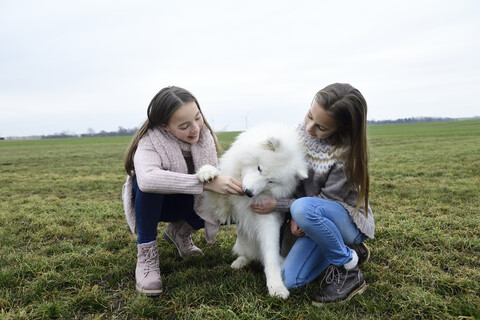 Zwei Mädchen hocken auf einer Wiese und lehren einen Hund, lizenzfreies Stockfoto