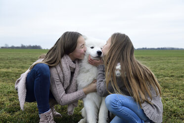 Zwei Mädchen kauern auf einer Wiese und küssen einen Hund - ECPF00266