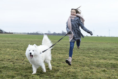 Lachendes Mädchen, das mit ihrem Hund auf einer Wiese läuft - ECPF00270