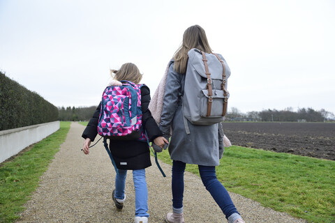 Rückenansicht von zwei Schwestern mit Rucksäcken, die Hand in Hand gehen, lizenzfreies Stockfoto