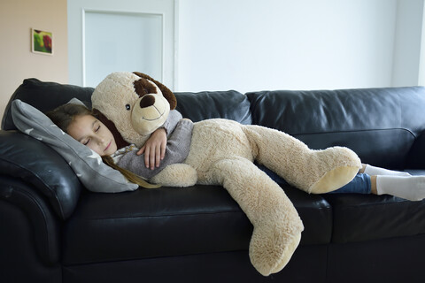 Mädchen entspannt auf Couch mit übergroßem Stofftier, lizenzfreies Stockfoto