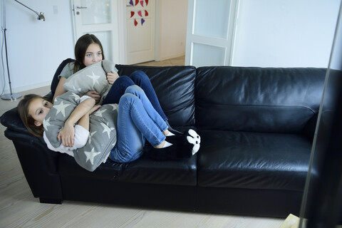 Two sisters watching television on couch stock photo