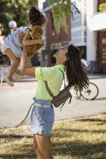 Happy mother lifting up daughter outdoors in the city - MAUF02397