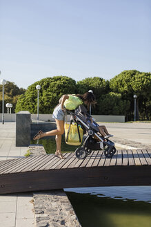 Mother with daughter in pram crossing wooden bridge in a park - MAUF02399