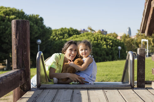 Smiling mother with daughter on slide on a playground - MAUF02402