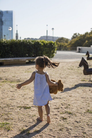 Rear view of little girl with teddy on a playground stock photo