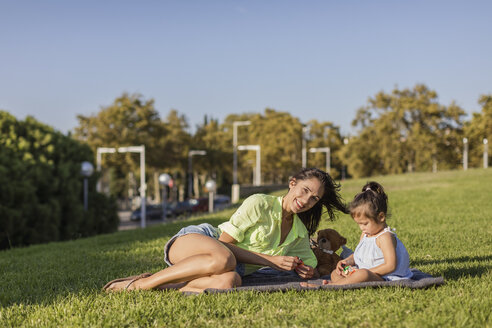 Happy mother playing with daughter on a blanket in park - MAUF02414