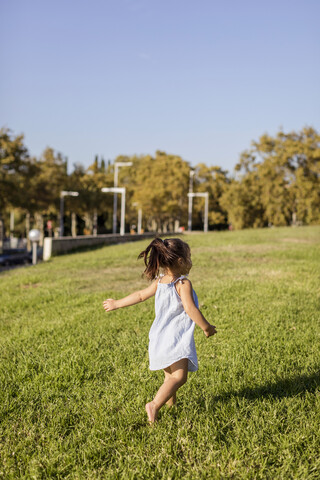 Rear view of little girl running on lawn in apark stock photo