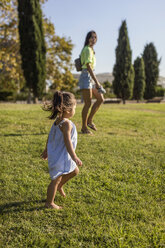Little girl walking on lawn in a park with her mother - MAUF02416