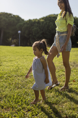 Kleines Mädchen, das mit seiner Mutter auf dem Rasen in einem Park spazieren geht, lizenzfreies Stockfoto