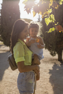 Mother explaining daughter leaf of a tree in park - MAUF02421