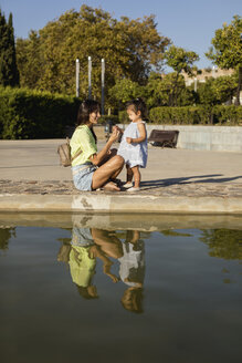 Happy mother with daughter at a pool in a park - MAUF02423