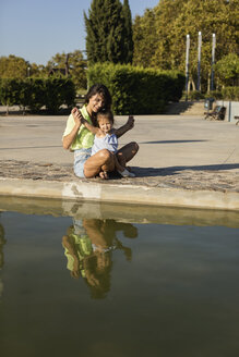 Happy mother with daughter at a pool in a park - MAUF02424