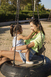 Glückliche Mutter mit Tochter auf Reifenschaukel auf einem Spielplatz - MAUF02429