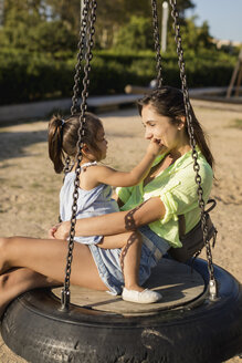 Happy mother with daughter on tire swing on a playground - MAUF02429