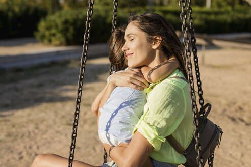 Lächelnde Mutter, die ihre Tochter auf einem Spielplatz umarmt - MAUF02431