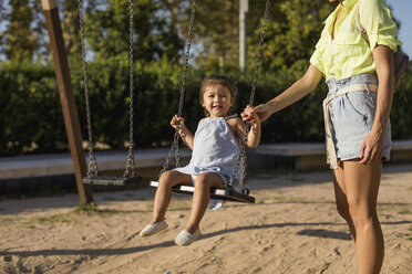 Mother holding daughter's hand swinging on a playground - MAUF02433